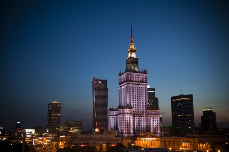 The illuminated Palace of Culture and Science towering over the Warsaw, Poland skyline at dusk.
