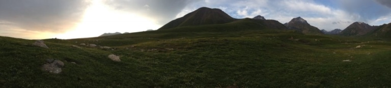 A panoramic view of green mountain slopes at dusk in Kyrgyzstan.