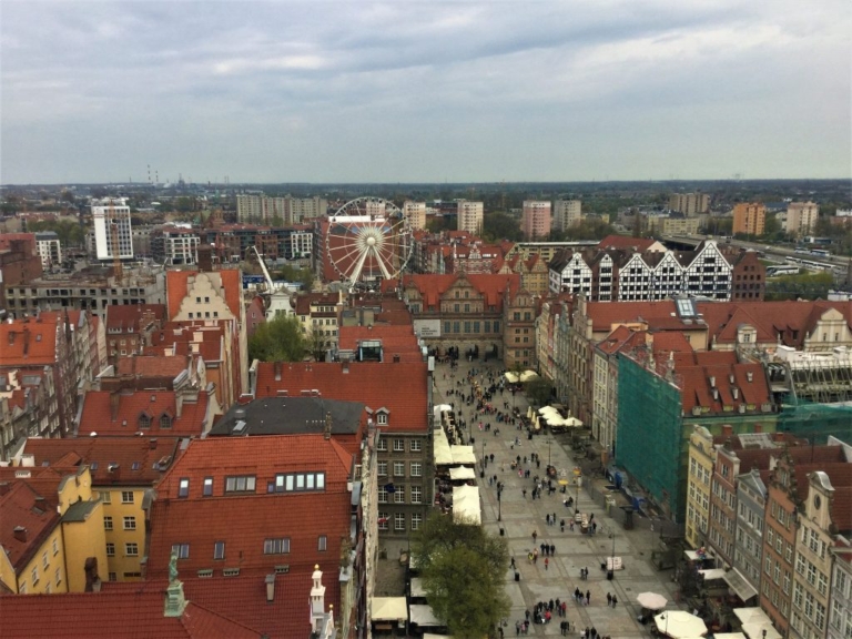 Aerial view of a European old town square with a Ferris wheel and red-tiled rooftops.