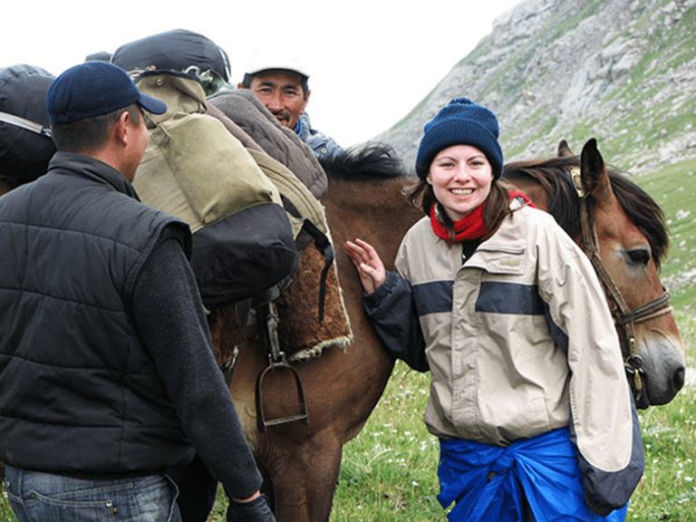 A student petting a horse while local guides look on in a green mountain valley in Kyrgyzstan.