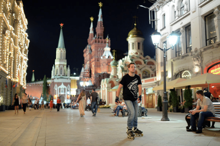 A man rollerblading on a pedestrian street near St. Basil's Cathedral and the Kremlin at night.