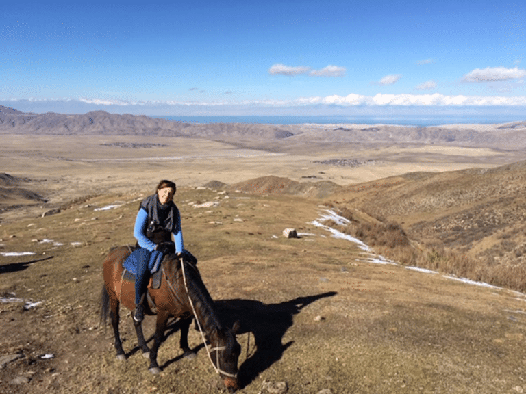 A student on horseback overlooking a mountain valley and lake in Kyrgyzstan.