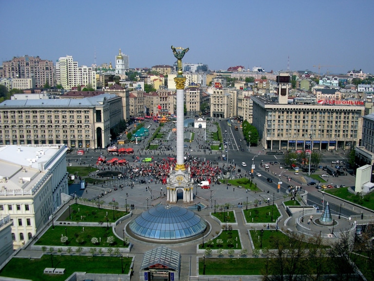 Aerial view of Independence Square in Kyiv, Ukraine, with the Independence Monument column and a crowd gathered below.