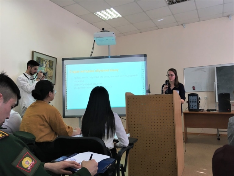 Student giving presentation in classroom as other students look on.