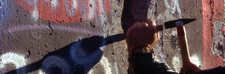 Close-up of hands chipping paint-covered concrete from the Berlin Wall.