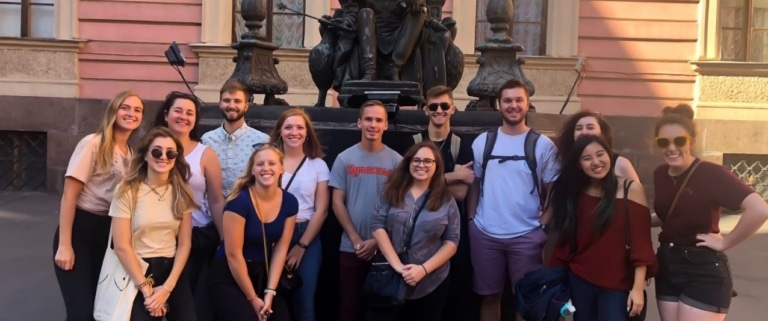 A group of students posing in front of a statue outside a pink building in St. Petersburg.