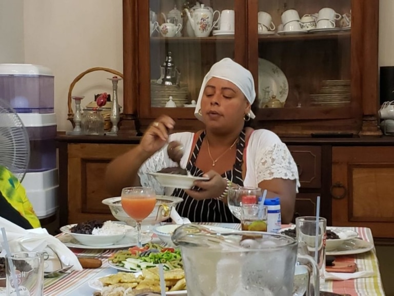 A woman in a white headscarf enjoying a spread of Cuban food, including rice, beans, and fried plantains.
