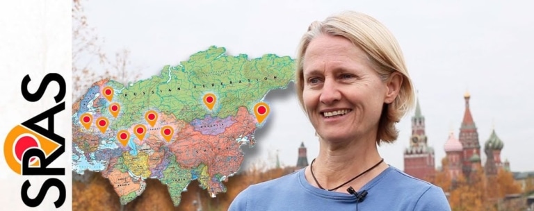 Renee Stillings smiling beside a map of the Russian Federation marked with SRAS program locations, with the SRAS logo and the Kremlin in the background.