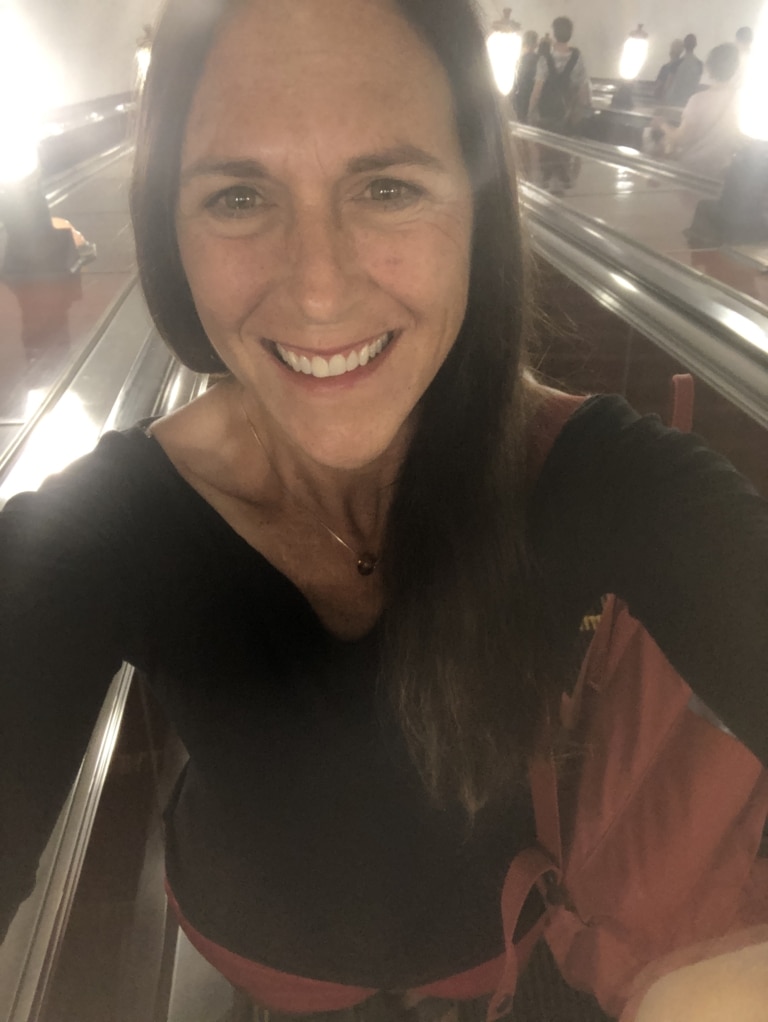 Molly Cain smiling in a selfie on a Moscow metro escalator.