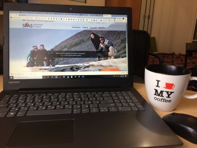 A laptop displaying the SRAS website homepage next to a coffee mug on a desk.