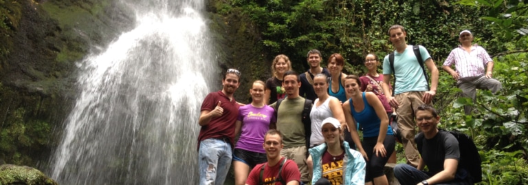 A group of students pose together in front of a waterfall while hiking in Georgia.