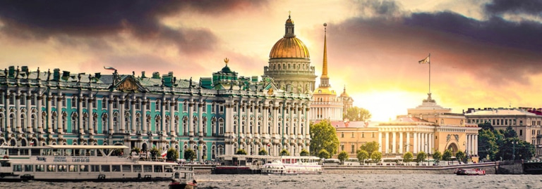 The Winter Palace, Hermitage, and St. Isaac's Cathedral skyline in St. Petersburg at sunset, viewed from the Neva River.