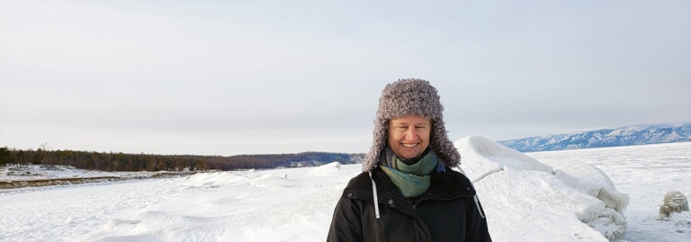 Woman in a fur hat smiling on the frozen, snow-covered shore of Lake Baikal.
