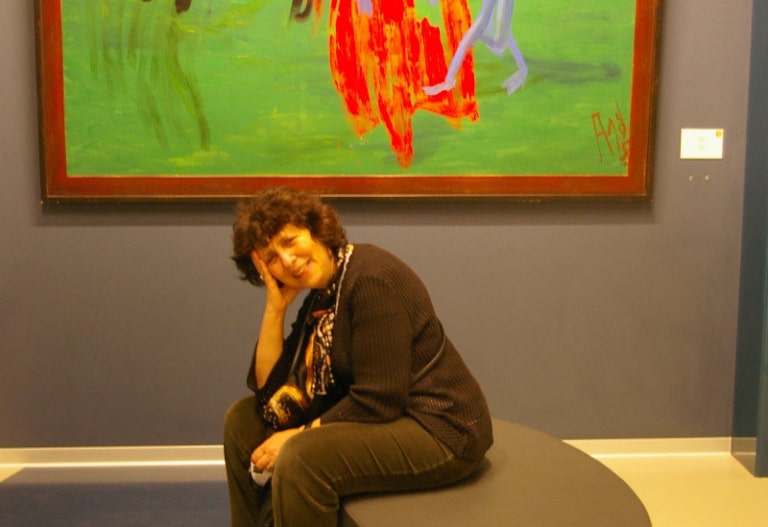 A woman leaning her head on her hand while sitting on a bench beneath a red and green abstract painting.