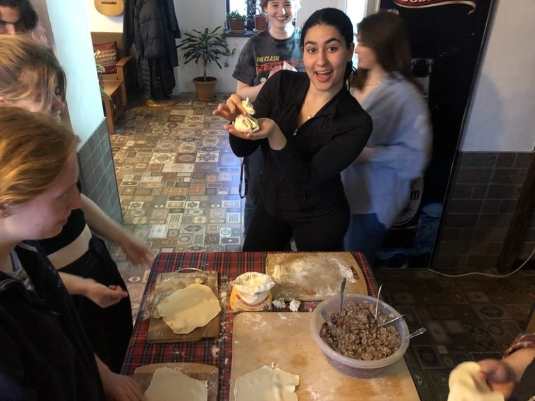 A student holding up a Georgian khinkali dumpling while cooking with a group in a kitchen.