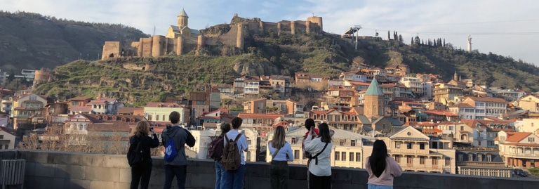 A group of students photographing the Narikala Fortress and Tbilisi's old town skyline in Georgia.