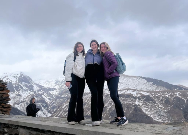 Three students posing together on a mountaintop with snow-capped peaks in the background in Georgia.