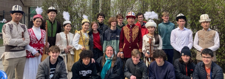 A group of students posing with performers in traditional Kyrgyz costumes outdoors.