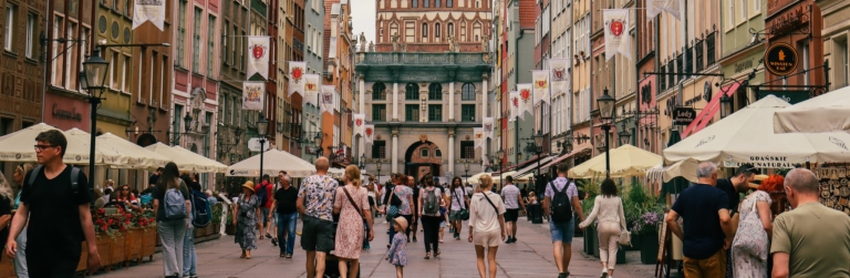 A crowded pedestrian street lined with colorful buildings and cafes in Gdansk's Long Market, Poland.