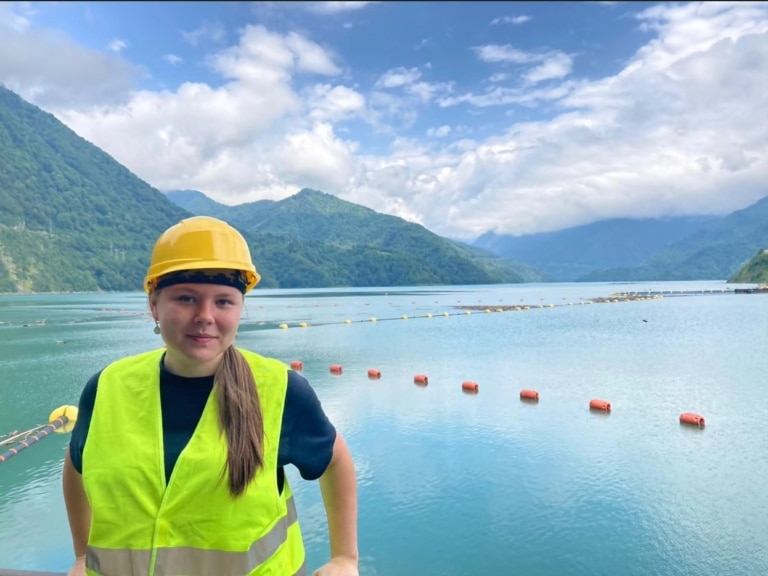 A woman wearing a hard hat and safety vest in front of the Enguri reservoir in Georgia.