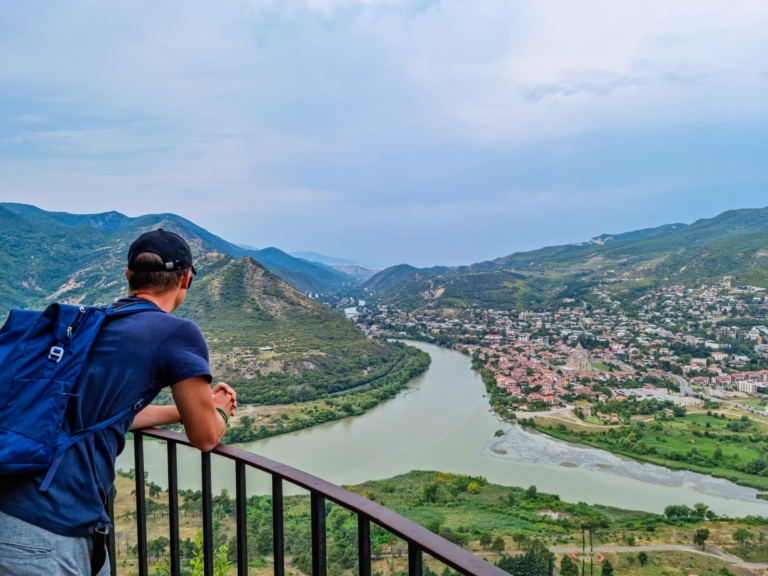 A man wearing a backpack looking out over the Mtkvari and Aragvi river confluence and the town of Mtskheta, Georgia.
