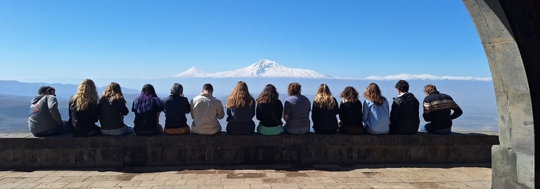 A group of students sitting on a wall overlooking Mount Ararat in Armenia.