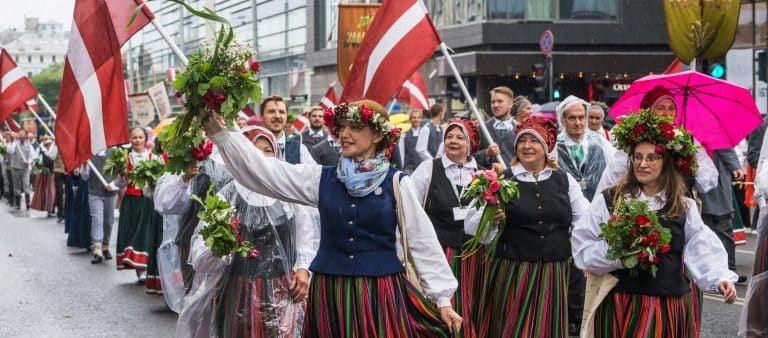 This image shows participants in traditional Latvian folk costumes marching in a festive parade during the Latvian Song and Dance Festival in Riga, Latvia.