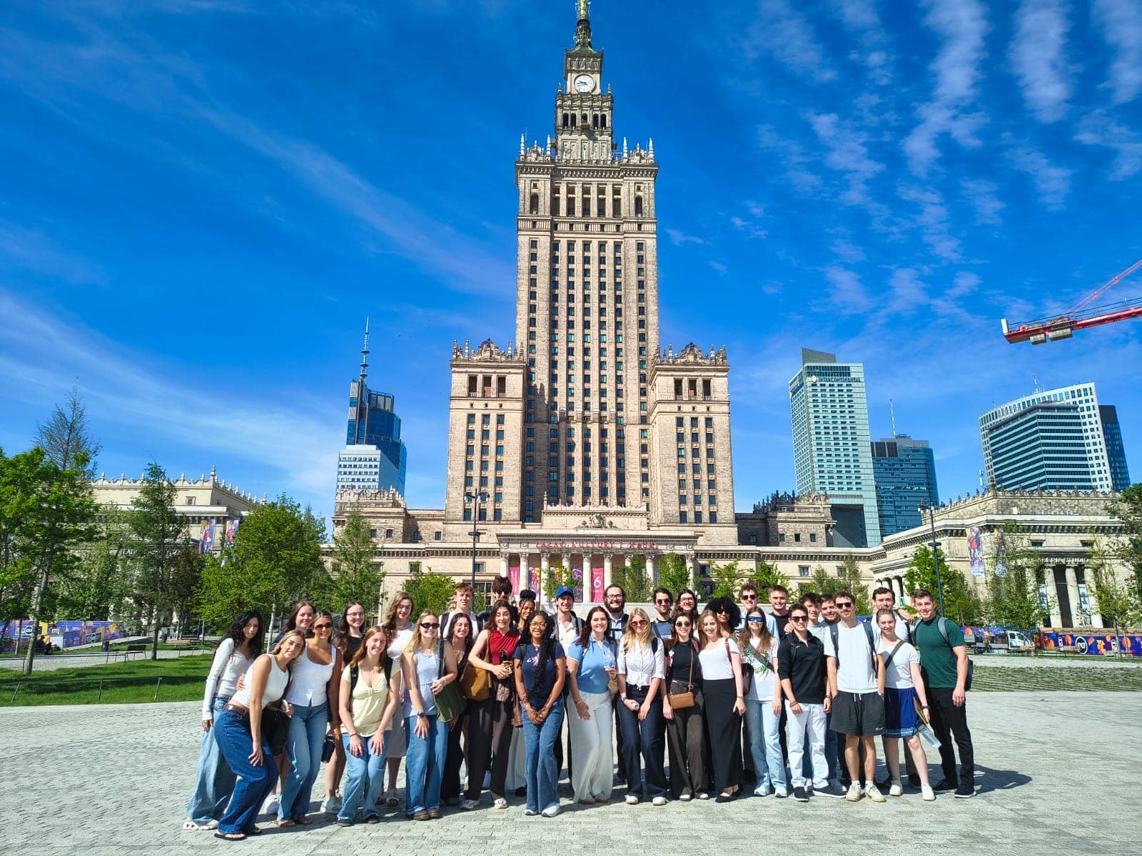 Group of students and faculty posing in front of historic European-style stone building with clock tower.