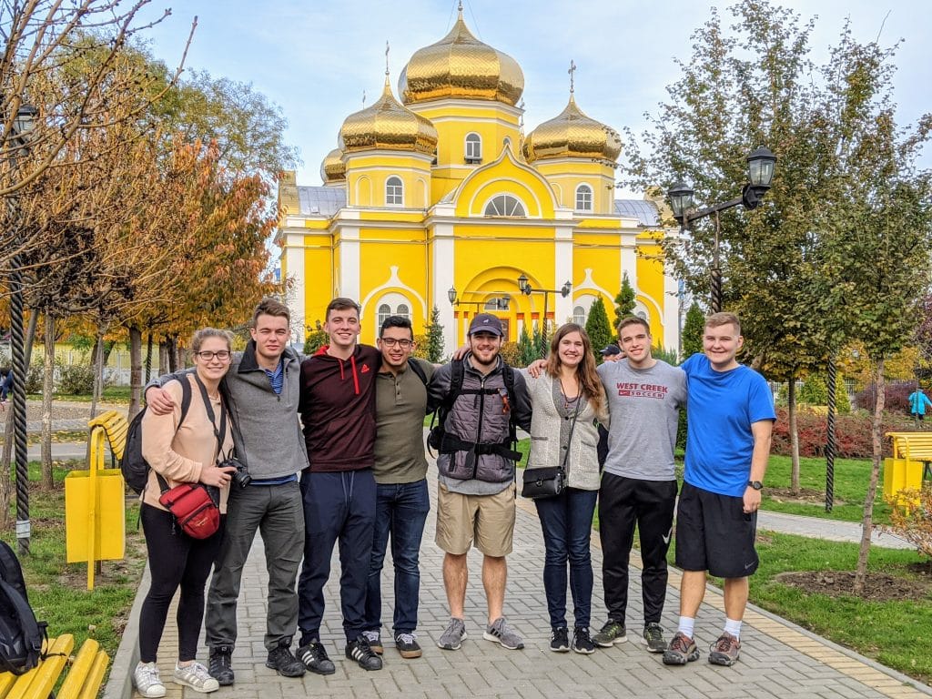 Group of smiling students in front of bright yellow domed building.