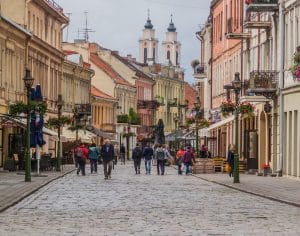 People walking away from camera on cobblestone street amidst colorful historic buildings.