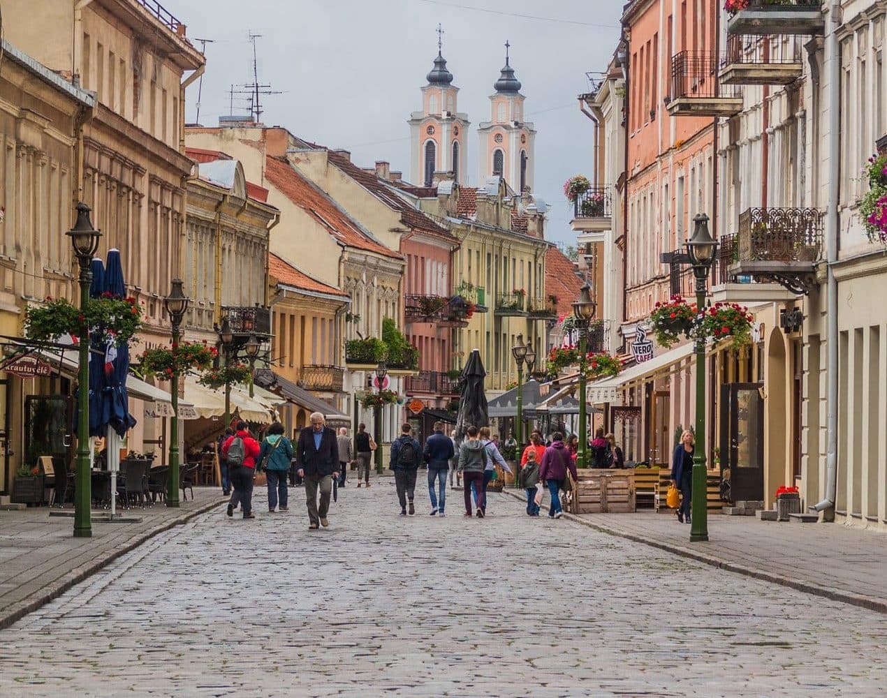 People walking away from camera on cobblestone street amidst colorful historic buildings.