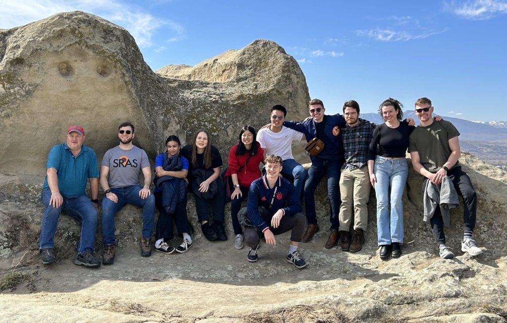 Group of smiling students standing on rocky mountaintop.