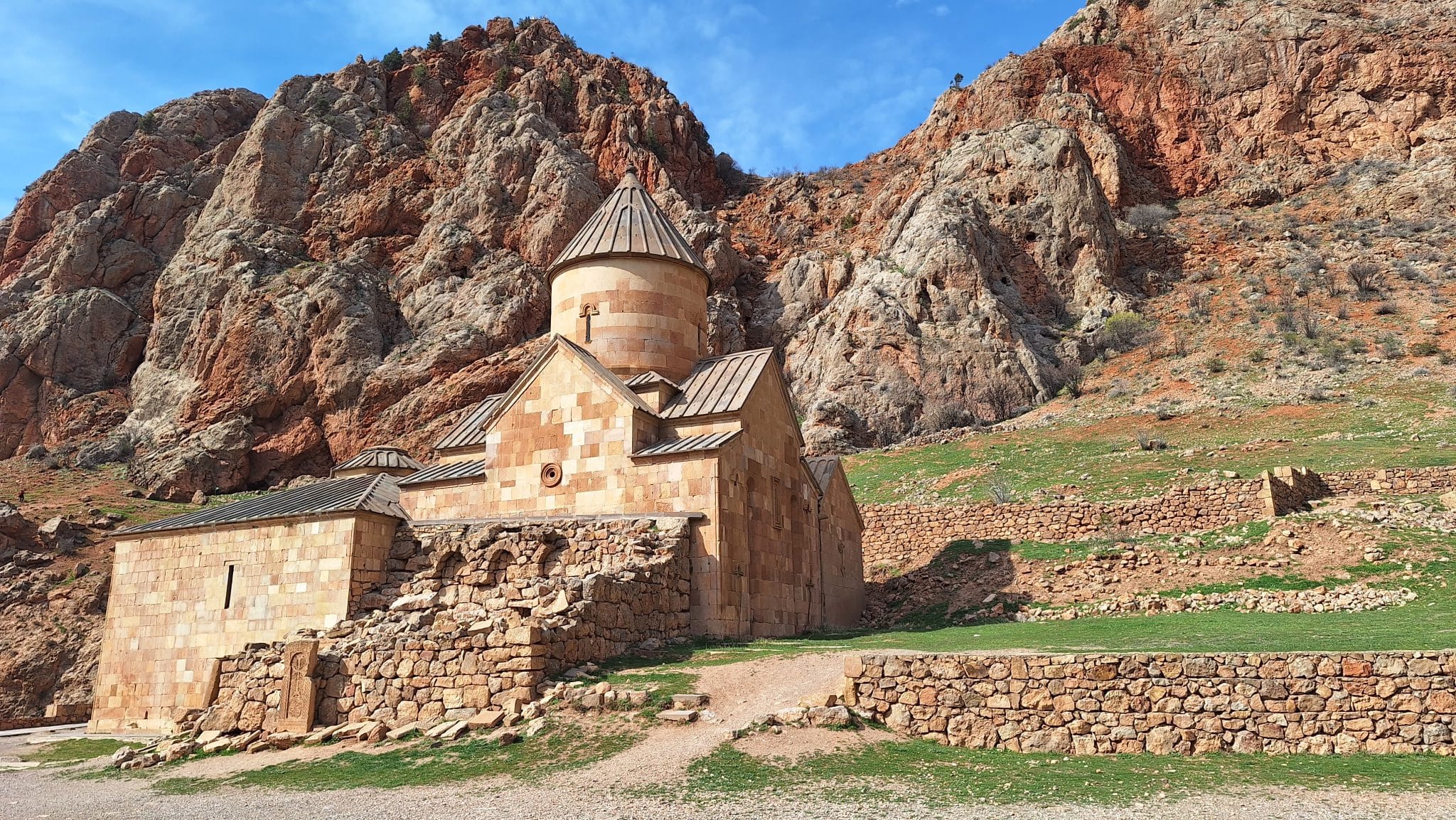 The image shows the 13th-century Noravank Monastery, nestled against dramatic brick-red cliffs in the Amaghu Gorge near Yeghegnadzor, in the Vayots Dzor Province of Armenia.