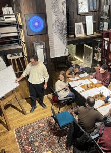 Teacher demonstrating Georgian calligraphy to students in cozy classroom.