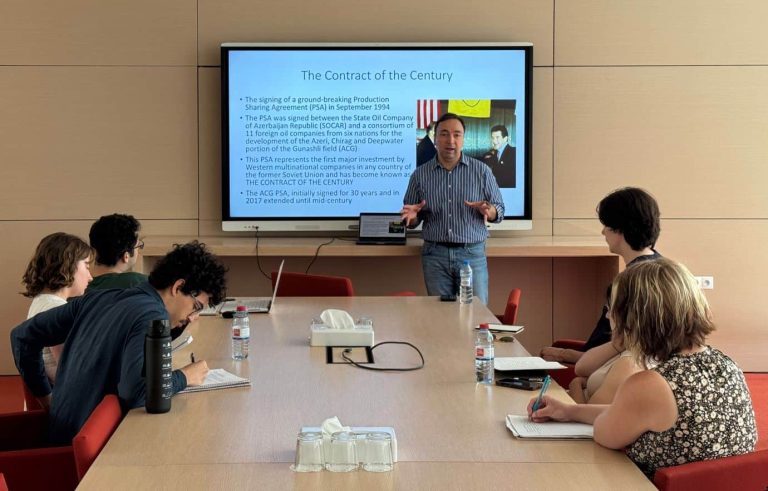 Professor giving lecture to students with presentation titled 'The Contract of the Century' behind him.