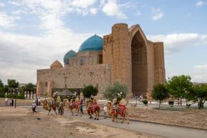 The Khoja Ahmed Yasawi Mausoleum in the city of Turkestan. Tourists ride camels in the foreground. Travel to Turkestan. Tourism in Kazakhstan.