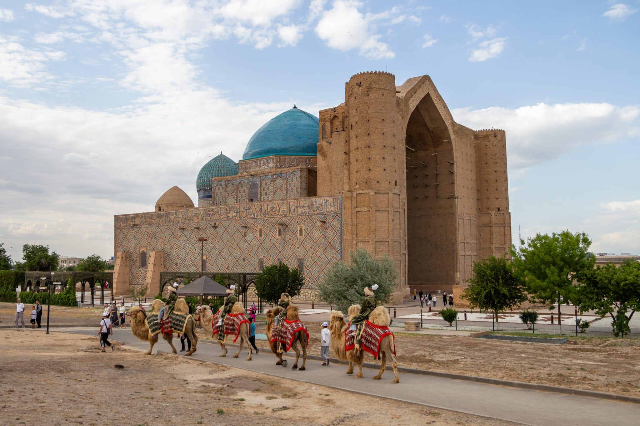The Khoja Ahmed Yasawi Mausoleum in the city of Turkestan. Tourists ride camels in the foreground. Travel to Turkestan. Tourism in Kazakhstan.