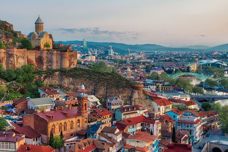 Overhead view of colorful city buildings overlooked by an old stone fortress on a hilltop.