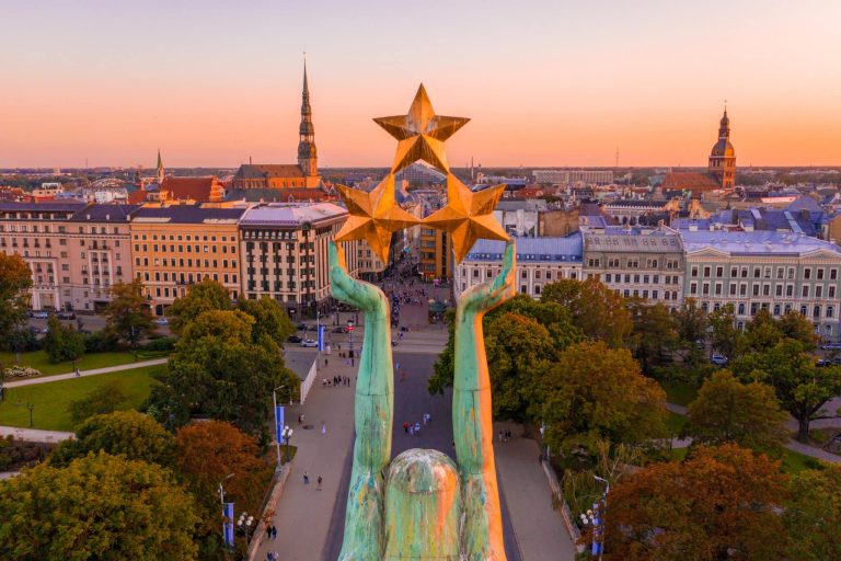 View of statue holding up 3 stars with city at sunset in background.