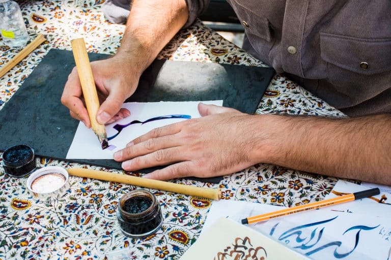 Close-up of hands drawing beautiful Persian letters.