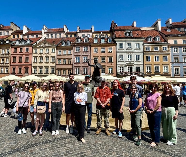 Students in Old Town Warsaw with the iconic Mermaid, a symbol of protection and security from Polish folklore.