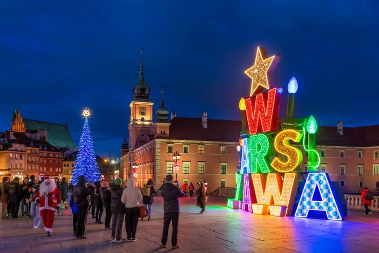 Illuminated Warszawa (Warsaw) sign and group of people on the Castle Square in the Old Town at night, Christmas time holiday season illumination.